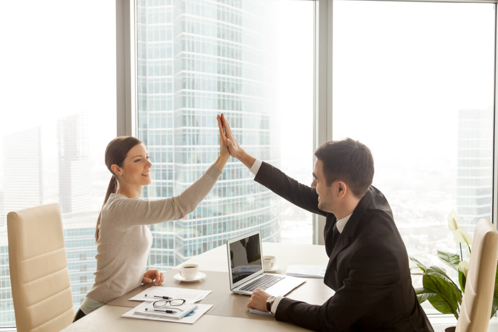 Businessman giving high five to businesswoman at office, partners celebrating good successful teamwork result, business team happy with job well-done, business achievement, company growth, side view