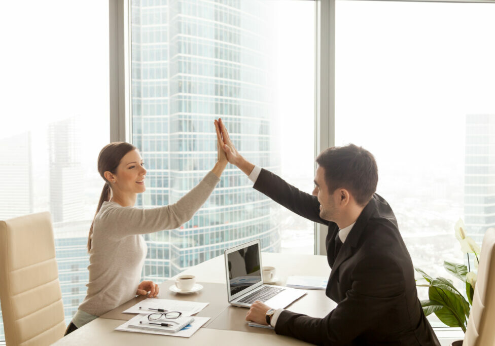 Businessman giving high five to businesswoman at office, partners celebrating good successful teamwork result, business team happy with job well-done, business achievement, company growth, side view